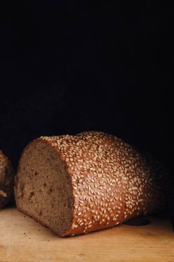 Koyu arkaplanda kesme tahtasına susam tohumları serpiştirilmiş çörek.