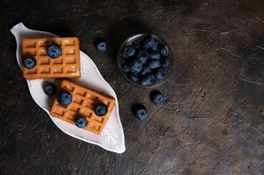 Koyu arkaplanda bir tabakta waffle ve yaban mersini.