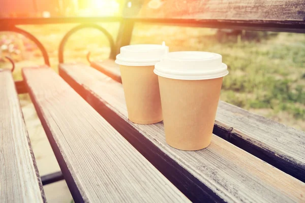 Two cups of coffee to take away in park on wooden bench in early morning with sunny glow