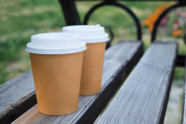 Two cups coffee to take away in park on wooden bench.