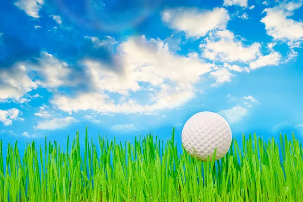 Golf ball on a green lawn against a blue sky with clouds