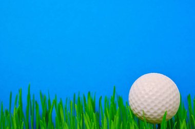 Golf ball on a green lawn on a blue background