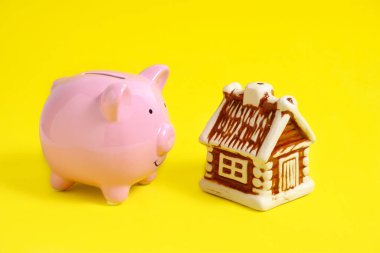 Sarı arka planda domuz kumbarası ve ev, konut kredisi tasarrufu kavramı