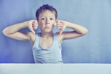 Oğlan tişörtle masada oturuyor ve hoşlanmadığını gösteriyor. Duygularının ifadeleri.