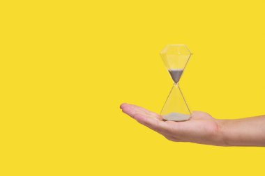 Avucunun içinde kum saati, sarı arka plan, kayıp konsepti ve yaşlılık zamanı.