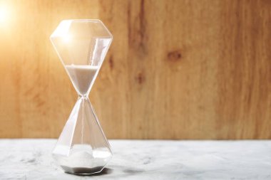 Parlak güneşli bir günde kum saati, ahşap arka planda pencere, zaman geçiyor