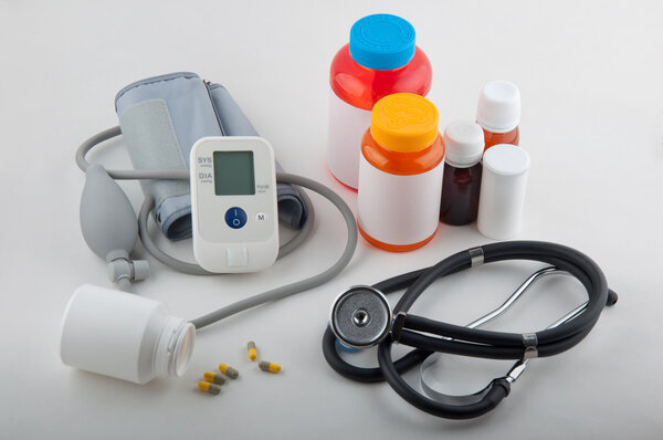 Grey medical tonometer, phonendoscope, pills and drug bottles on white