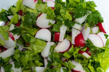 Taze bahar dilimlenmiş turp, yeşil salata yaprakları ve maydanoz beyaz bir tabakta yatıyor. Vejetaryen yemeği, vitamin kasesi. Kilo verme diyeti, üst görüş. Yüksek kalite fotoğraf