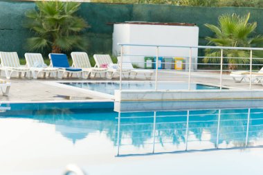 Temiz mavi suyu çevreleyen şezlonglar ve palmiye ağaçları ile yüzme havuzu boş ve rahat bir ortam yaratıyor. Yüksek kalite fotoğraf