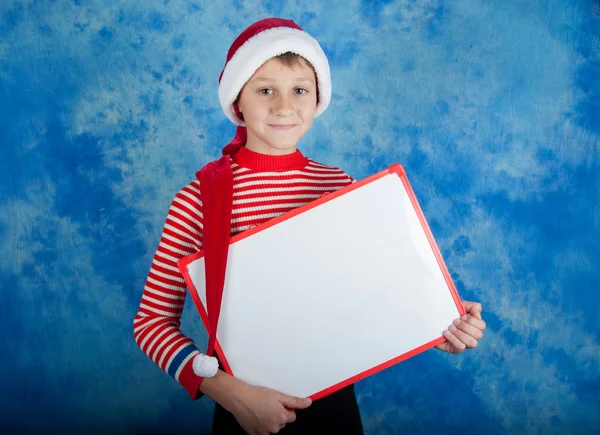 Niño feliz en Santa sombrero rojo sosteniendo tablero blanco — Foto de Stock