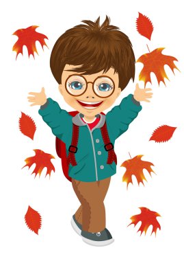 little boy with glasses and backpack playing with autumn leaves