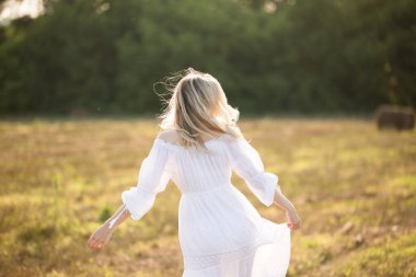 Tarlada dalgalı saçları olan beyaz elbiseli bir kız.