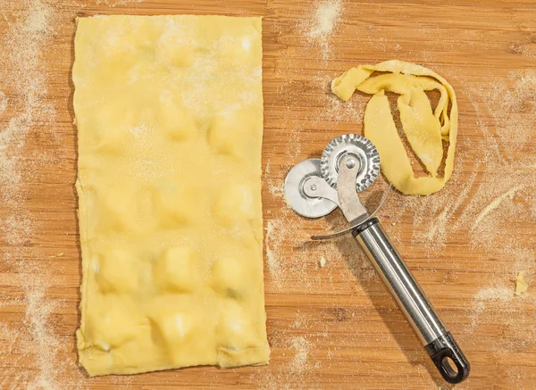 Ravioli caseiro e massa crua coberta com farinha.Cortador de massa de rodas colocado em uma mesa de madeira . — Fotografia de Stock