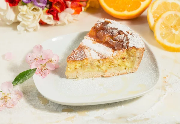 Um pedaço de torta napolitana de Páscoa polvilhada com açúcar de confeiteiro e decorada com flor de amêndoa, frésia e frutas frescas . — Fotografia de Stock