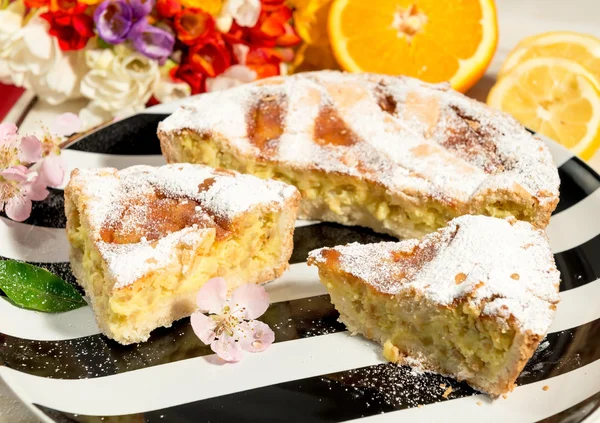 Un trozo de pastel napolitano de Pascua espolvoreado con azúcar glaseado y decorado con flor de almendras, freesia y frutas frescas . — Foto de Stock