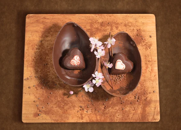 Ovo de chocolate de Páscoa com uma surpresa de dois corações decorados, polvilhados com cacau em pó, pedaços de chocolate e flor de amêndoa . — Fotografia de Stock