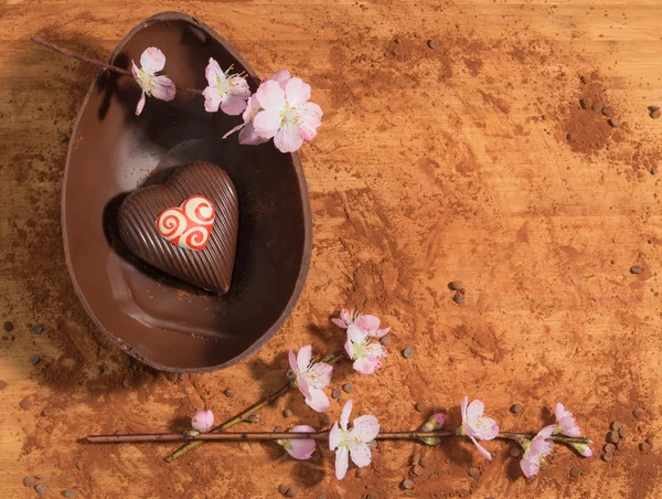 Ovo de chocolate de Páscoa com uma surpresa de coração de chocolate decorado, polvilhado com cacau em pó e acompanhado com flor de amêndoa . — Fotografia de Stock