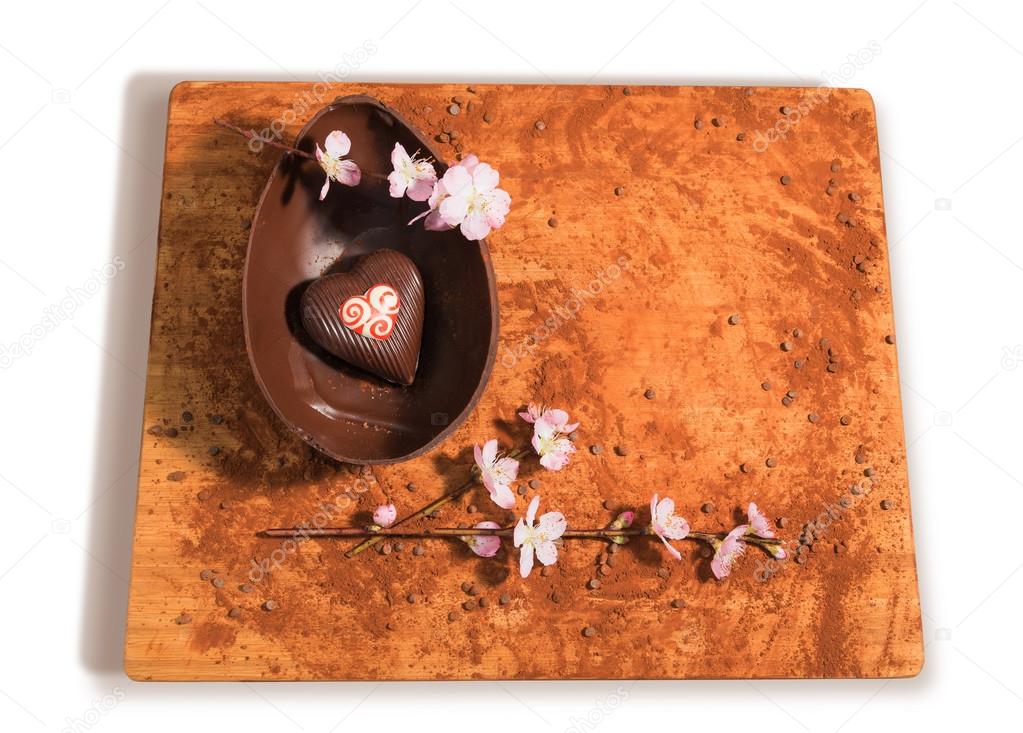 Easter chocolate egg with a surprise of a heart decorated,sprinkled with cocoa powder,chocolate chips and almond blossom.