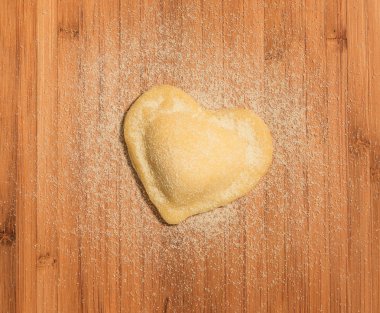 Ahşap bir masa üzerinde kalp şeklinde, ev yapımı tek raviolo yer.