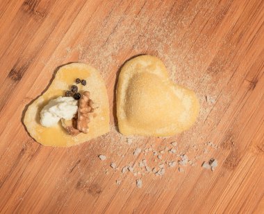 İki ev yapımı ravioli, açık ve kapalı, un serpilir ve ahşap bir masa üzerinde yerleştirilen kalp şeklinde.