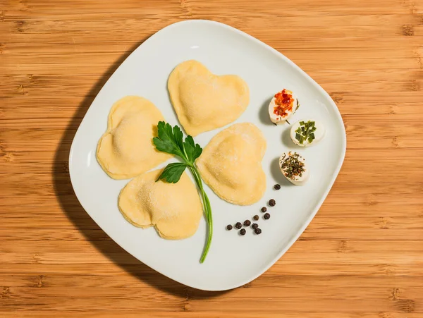Yonca dört kalp şeklinde, ev yapımı ravioli ile yapılan ve peynir aralıklı. Ahşap bir masa üzerinde beyaz çanak yerleştirilir.