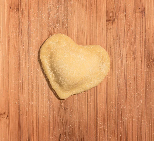 Ahşap bir masa üzerinde kalp şeklinde, ev yapımı tek raviolo yer.