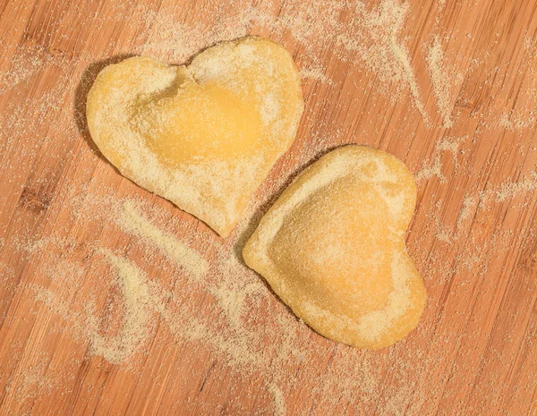 Two raw homemade ravioli in the shape of heart,sprinkled with flour and placed on a wooden table. — Stock Photo, Image