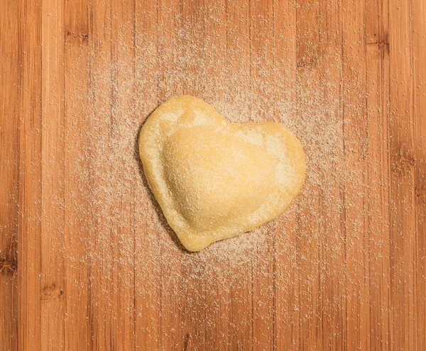 Ahşap bir masa üzerinde kalp şeklinde, ev yapımı tek raviolo yer.