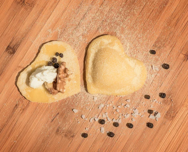 İki ham ev yapımı ravioli, açık ve kapalı, un serpilir ve ahşap bir masa üzerinde yerleştirilen kalp şeklinde.