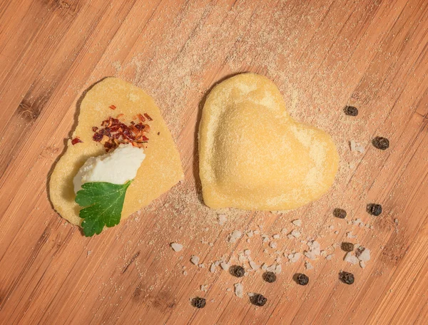 Two raw handmade ravioli in the shape of heart,open and closed,sprinkled with flour and placed on a wooden table. — Stock Photo, Image