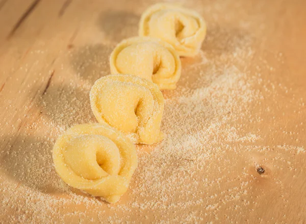 Tortellini caseiro italiano colocado sobre uma mesa de madeira polvilhada com farinha . — Fotografia de Stock