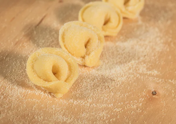 Tortellini casero italiano colocado en una mesa de madera espolvoreada con harina . — Foto de Stock