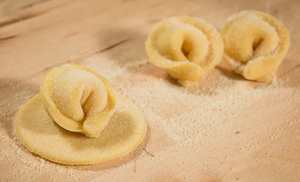 Tortellini casero italiano colocado en una mesa de madera espolvoreada con harina . — Foto de Stock