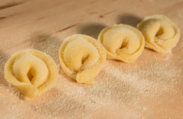 Tortellini casero italiano colocado en una mesa de madera espolvoreada con harina . — Foto de Stock