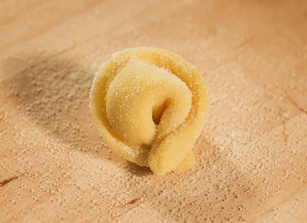 Tortellino caseiro italiano colocado sobre uma mesa de madeira polvilhada com farinha . — Fotografia de Stock