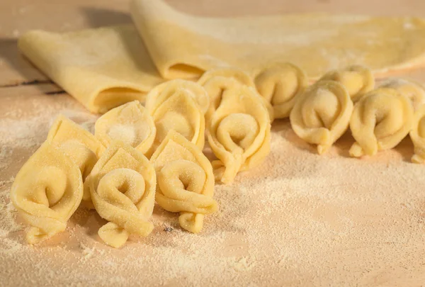Italienische hausgemachte Tortellini und roher Teig auf einem Holztisch mit Mehl bestreut. — Stockfoto