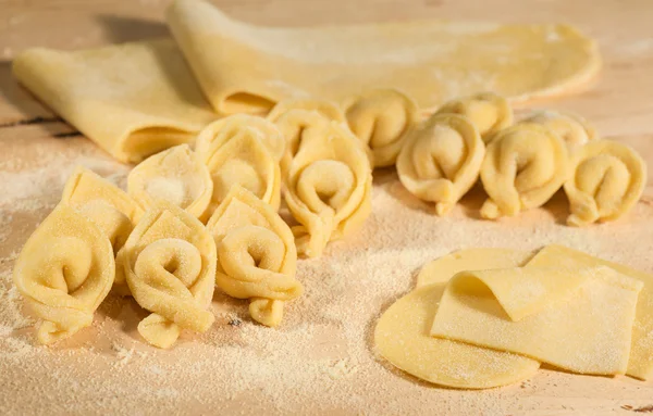 Italienische hausgemachte Tortellini und roher Teig auf einem Holztisch mit Mehl bestreut. — Stockfoto