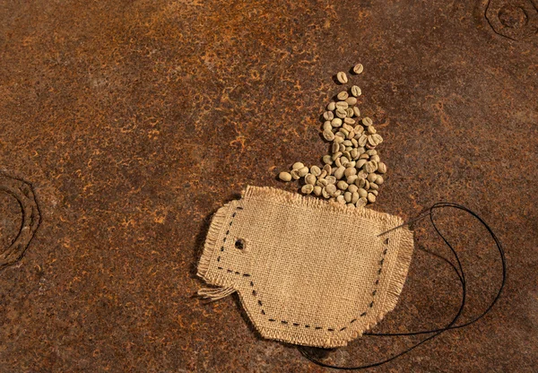 Uma xícara costurada em juta com agulha e arame cheio de grãos de café crus colocados em mesa enferrujada . — Fotografia de Stock