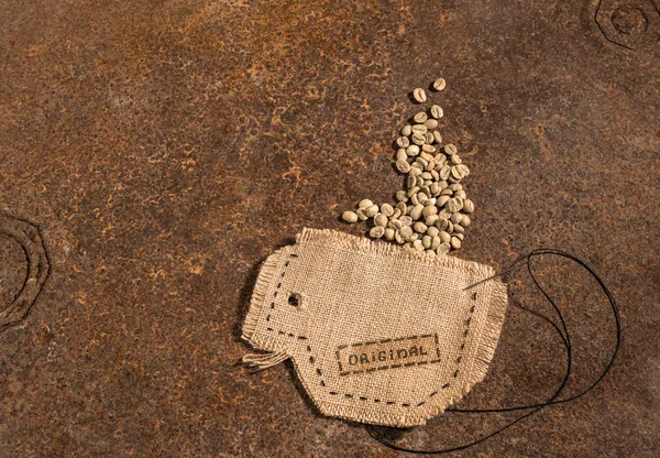 Een kopje genaaid in jute met naald en draad vol ruwe koffiebonen op roestig tafel geplaatst. — Stockfoto