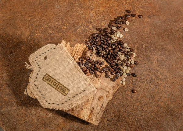 Eine aus Jute genähte Tasse voller Kaffeebohnen und altem Holz auf einem rostigen Tisch. — Stockfoto