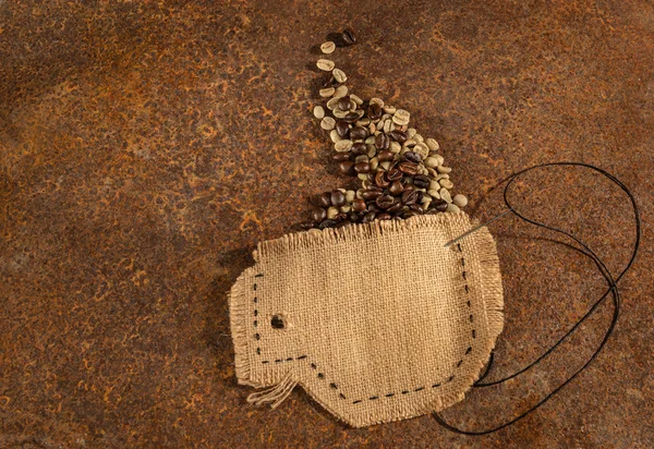 Een kopje genaaid in jute met naald en draad vol koffiebonen op roestig tafel geplaatst. — Stockfoto