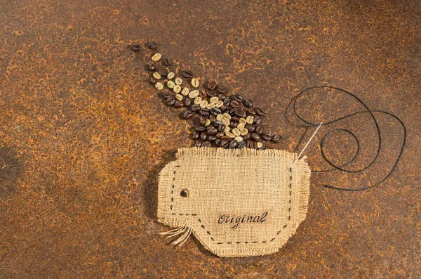 Una tazza cucita in iuta con ago e filo pieno di chicchi di caffè appoggiati su un tavolo arrugginito . — Foto Stock