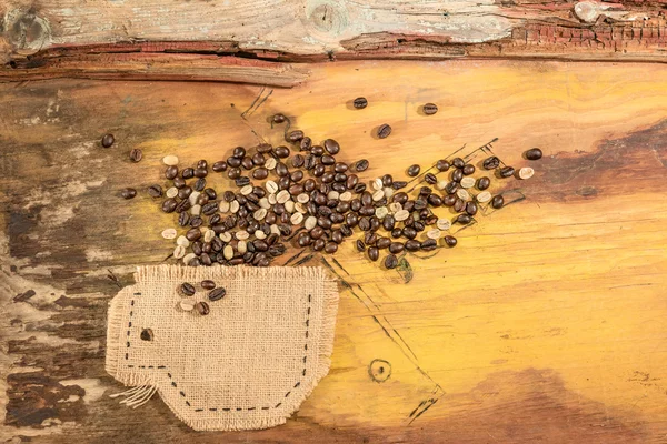 Una taza cosida en yute con granos de café colocados sobre una vieja mesa de madera . —  Fotos de Stock