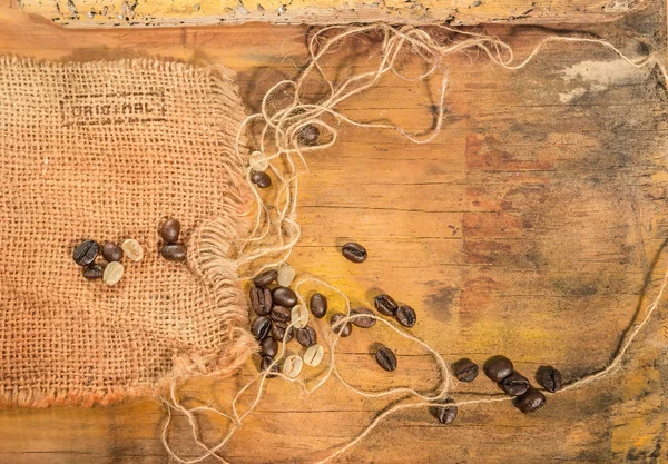 Grains de café crus et torréfiés placés sur jute et vieille table en bois . — Photo