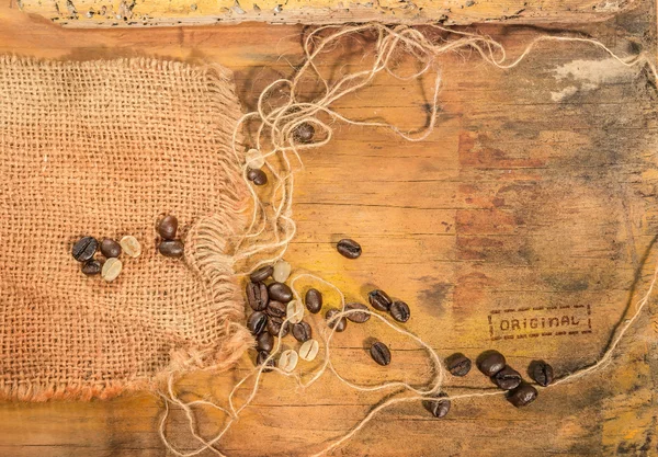 Chicchi di caffè crudi e tostati appoggiati su iuta e vecchio tavolo di legno . — Foto Stock