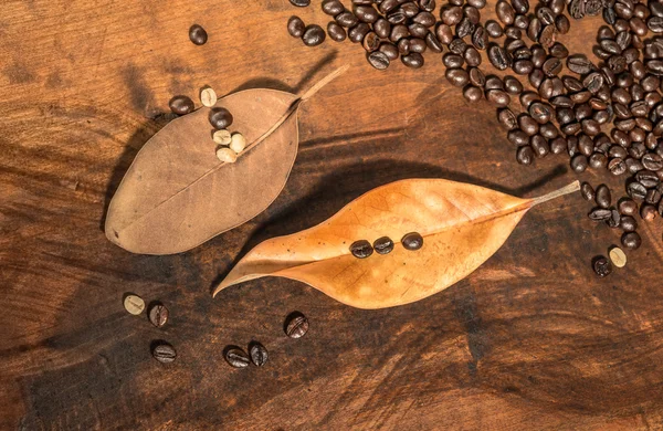 Coffee beans with dry leaves of magnolia placed on wooden table.