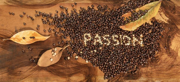 木製のテーブルの上に置かれたテキスト「情熱」と生とトーストコーヒー豆の心。マグノリアの乾燥した葉で飾られた. — ストック写真