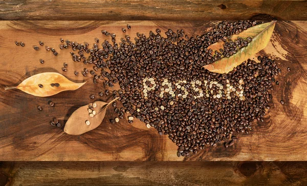 Un cœur de grains de café crus et grillés avec le texte "passion", placé sur une table en bois.Décoré de feuilles sèches de magnolia . — Photo