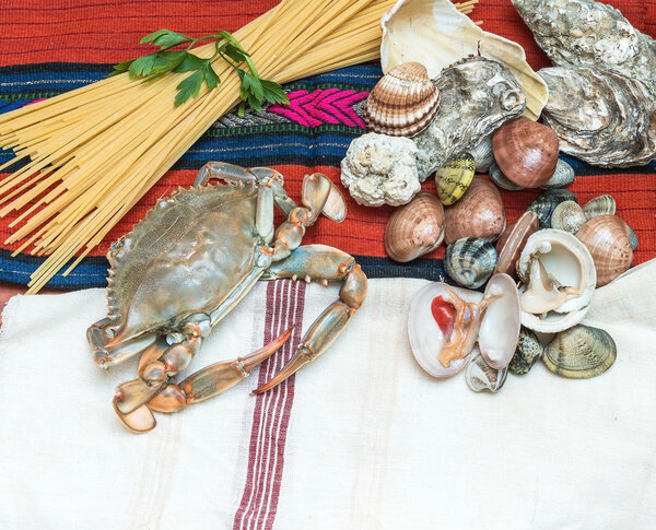 Краб, морепродукты со спагетти и раковины на этнической ткани
.