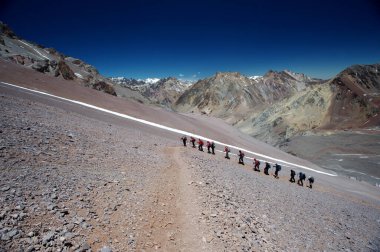 Karlı ve sarp dağlarda sıra sıra dağcıların aşırı koşullardaki hareketleri.